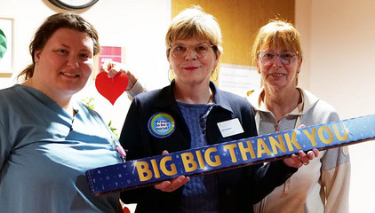 Sabine Kalkhoff, Gesamtleiterin Residenz am Wiesenkamp und Gesellschaft für Diakonie, hält mit zwei Mitarbeitenden ein Schild mit der Aufschrift "Big Big Thank You" in die Kamera am Internationalen Tag der Pflegenden in Hamburg-Volksdorf.